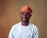 Smiling man in Nigerian attire and a cap with a warm, neutral background.