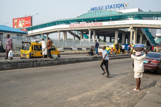 Street hustle at Mile 2 Station with yellow buses and pedestrians in Lagos, Nigeria.